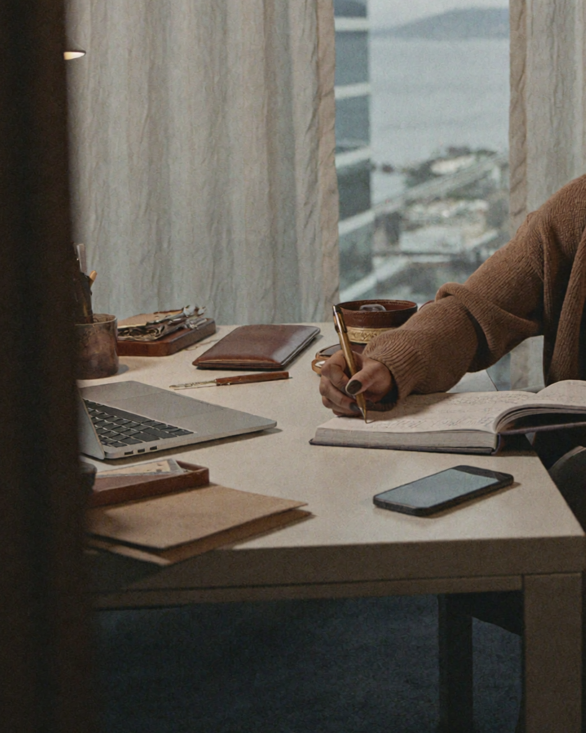 Founder writing in a notebook at a desk with a laptop, camera, and unedited content nearby